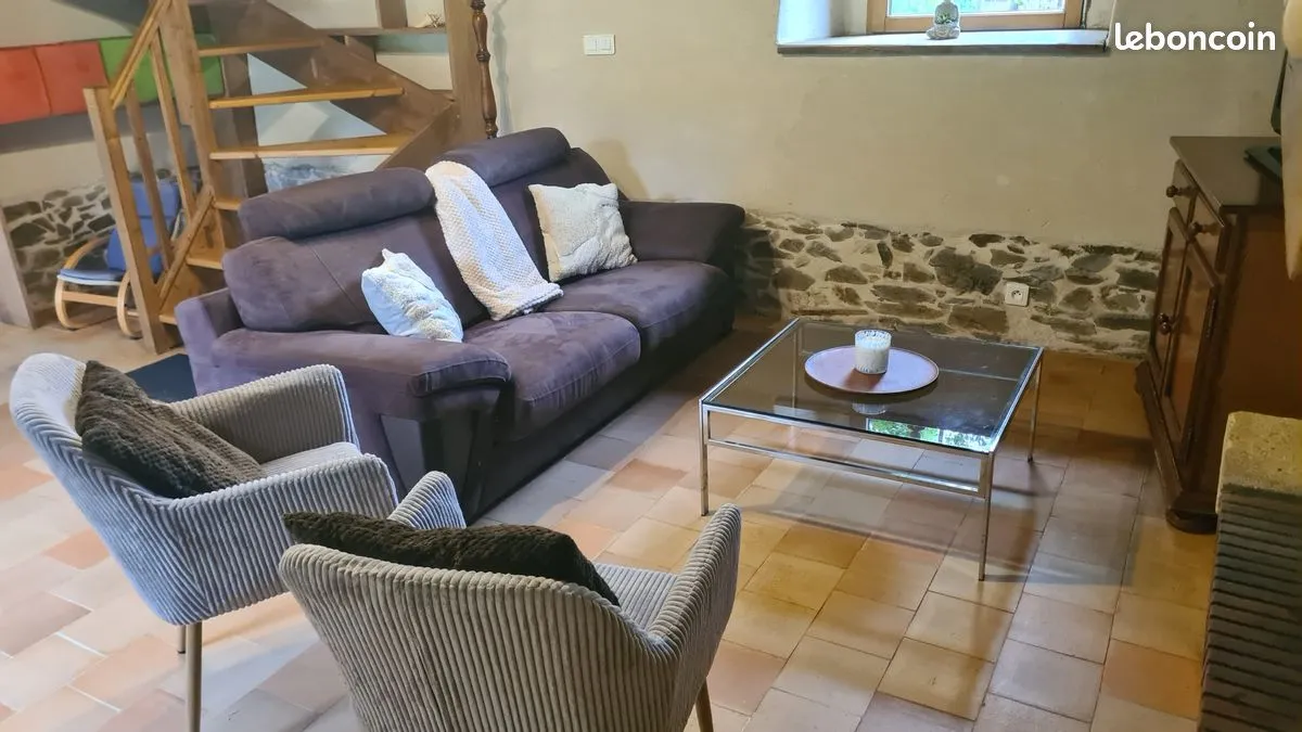 Coin salon du gîte avec mur en pierre apparente et fauteuils